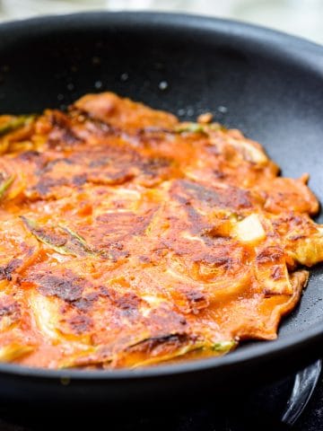 Kimchi pancake being pan fried in a non-stick pan