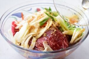 thinly sliced beef and vegetables being mixed with the marinade