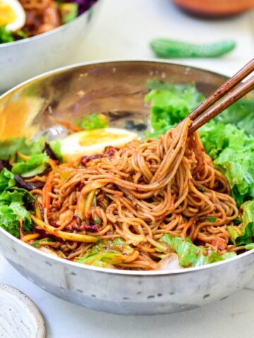 Cold buckwheat noodles and vegetables mixed in a spicy gochujang sauce