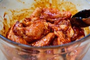 Chicken wings marinade in a red spicy sauce in a pyrex bowl