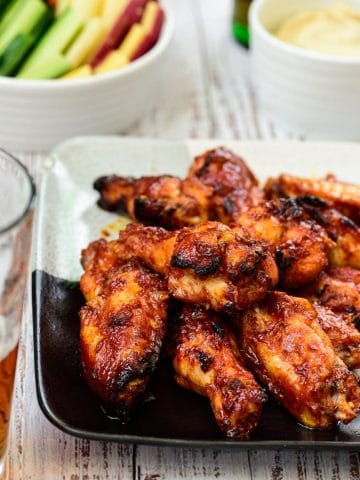 Red spicy baked chicken wings on a plate with vegetable sticks in the background