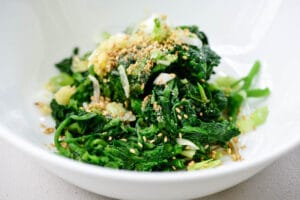 Blanched and squeezed watercress being seasoned in a bowl