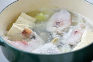 boiling cod fish, tofu and clams in a clear broth