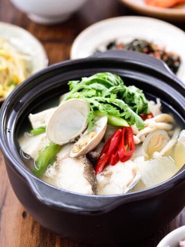 Korean mild cod fish stew in an earthen pot served with various side dishes