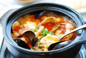 red spicy extra tofu stew with an assortment of seafood in an earthen pot