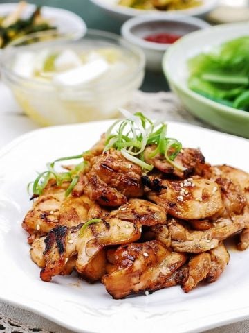 Chicken bulgogi on a plate with side dishes in the background