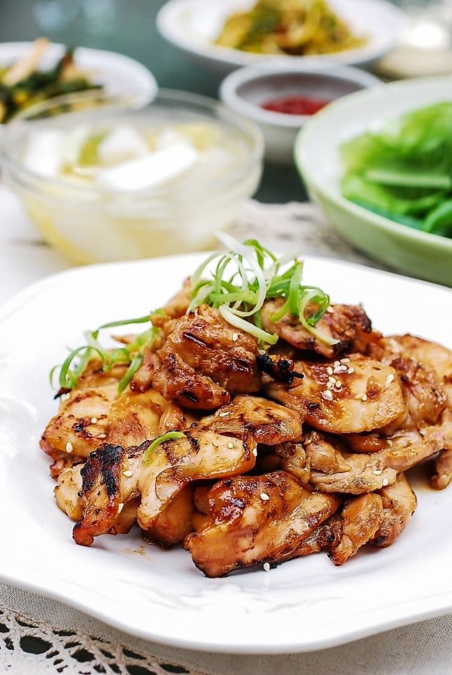 Chicken bulgogi on a plate with side dishes in the background