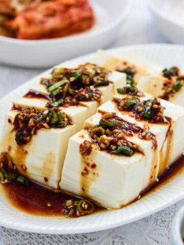 boiled tofu served with a soy based sauce drizzled on top alongside other Korean side dishes
