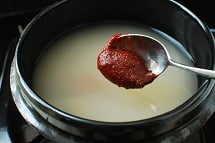 a tablespoon of gochujang being added to the broth in an earthenware