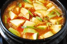 Potato and zucchini cut pieces in red spicy gochujang broth in an earthenware