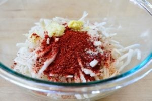 Julienned radish being mixed with Korean chili pepper powder