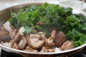 Kale and mushrooms being stir fried with chicken