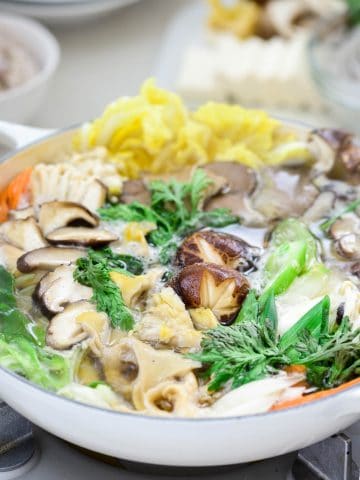 Korean hot pot with an assortment of mushrooms and other veggies in a shallow white pot