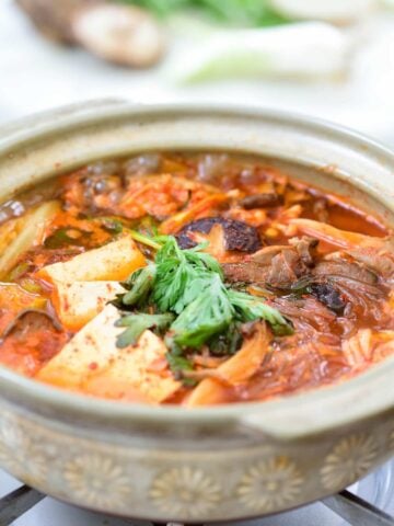 Red spicy mushroom stew with tofu and noodles in an earthenware over the stove