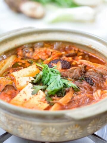Red spicy mushroom stew with tofu and noodles in an earthenware over the stove