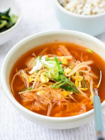 Red spicy soup with kimchi and soybean sprouts served with a bowl of rice