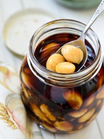 Soy pickled garlic cloves in a mason jar with a spoon holding a few in the jar