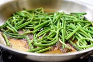 stir-frying garlic scapes in a sauce