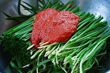 Kimchi seasoning being applied to garlic chives