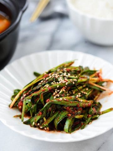 Korean garlic chive kimchi in a small plate served with a bowl of rice