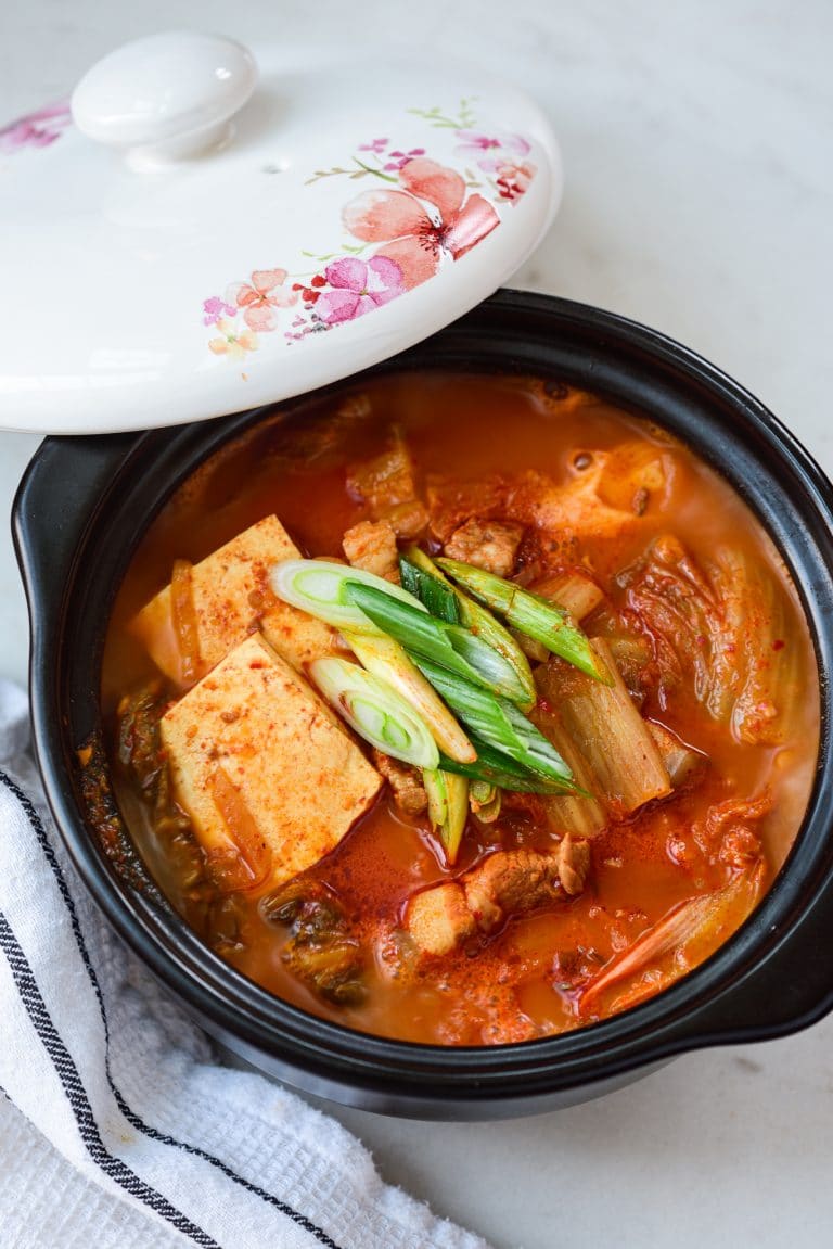 kimchi stew with tofu in an earthen pot with the lid laid on the side of the pot