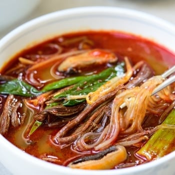 Korean red spicy soup with shredded beef, scallions, mushrooms and noodles in a large bowl
