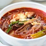 Korean red spicy soup with shredded beef, scallions, mushrooms eggs and noodles in a large bowl