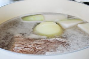 Boiling beef brisket in a large pot along with onion and Korean radish