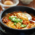 Red spicy soft tofu stew in an earthenware with a raw egg served in a separate bowl