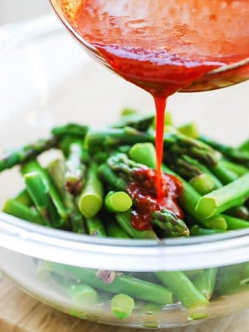 Red spicy gochujang sauce being poured over cut and blanched asparagus