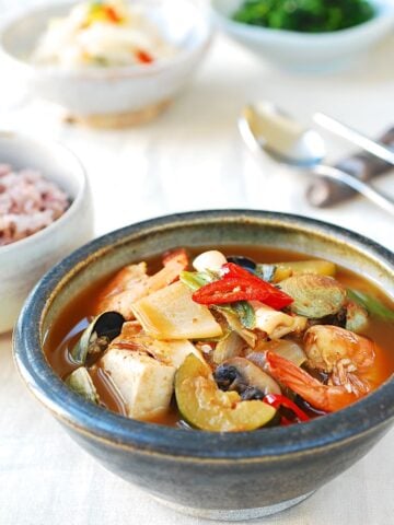 Seafood doenjang jjigae in a small bowl served with rice and vegetable side dishes