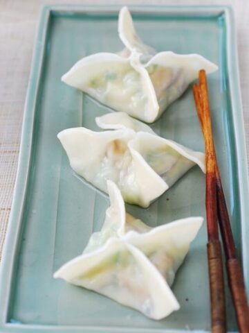 Three boiled zucchini dumplings in square or star shape on a green rectangle shape plate