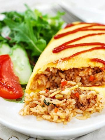 Fried rice wrapped in egg omelette drizzled with ketchup and served with lettuce, cucumber and tomato pieces