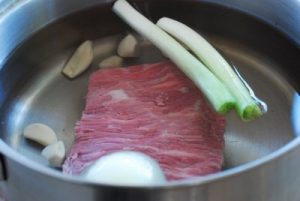 a large chunk of beef brisket in a pot with onion, garlic and scallions in a pot for making rice cake soup recipe