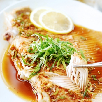 Hongeojjim (steamed skate fish) served in a large white plate, a piece being picked up with chopsticks