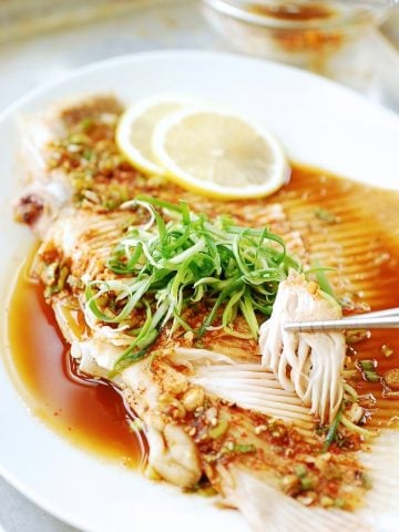 Hongeojjim (steamed skate fish) served in a large white plate, a piece being picked up with chopsticks