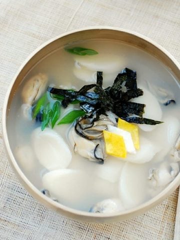 Korean rice cake soup made with oysters garnished with eggs and seaweed sheet