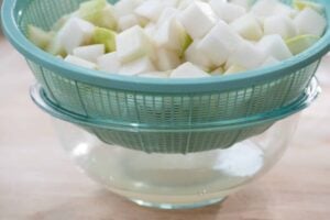 salted radish cubes being drained in a colander over a bowl