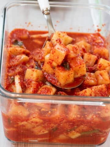cubed radish kimchi in a glass container with a spoonful being taken out