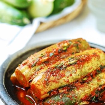 Stuffed cucumber kimchi in a plate with fresh cucumbers in the background