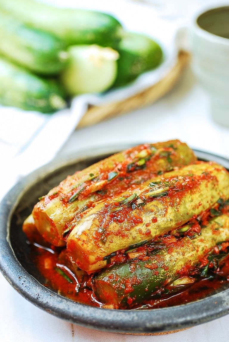 Stuffed cucumber kimchi in a plate with fresh cucumbers in the background