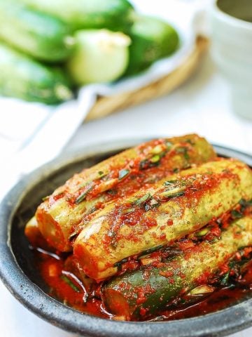 Stuffed cucumber kimchi in a plate with fresh cucumbers in the background