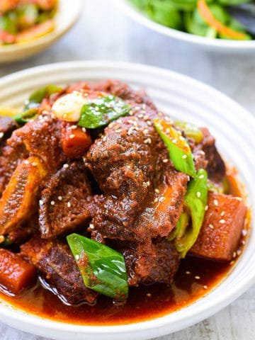 Red spicy braised short ribs with vegetables in a white plate