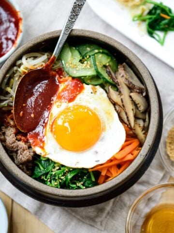 Bibimbap served with a sunny side up fried egg in an earthenware with a gochujang sauce on top