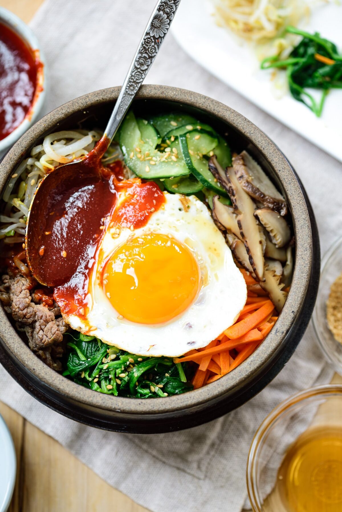 Bibimbap served with a sunny side up fried egg in an earthenware with a gochujang sauce on top
