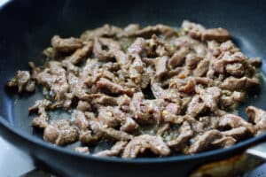cooking beef strips in a pan for Korean rice rolls