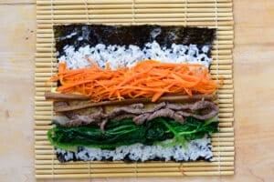 placing kimbap fillings on a seaweed with rice