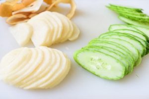 Thinly sliced pear and cucumbers on a cutting board