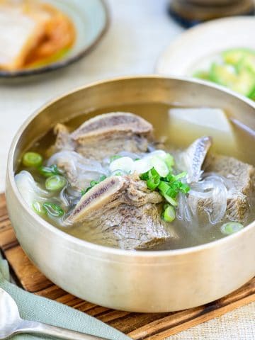 Beef short rib soup in a brass bowl with kimchi and zucchini side dish