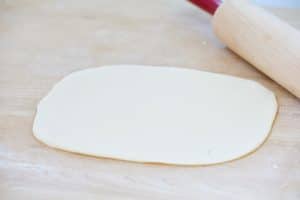 Rolled dough on a cutting board with a rolling pin